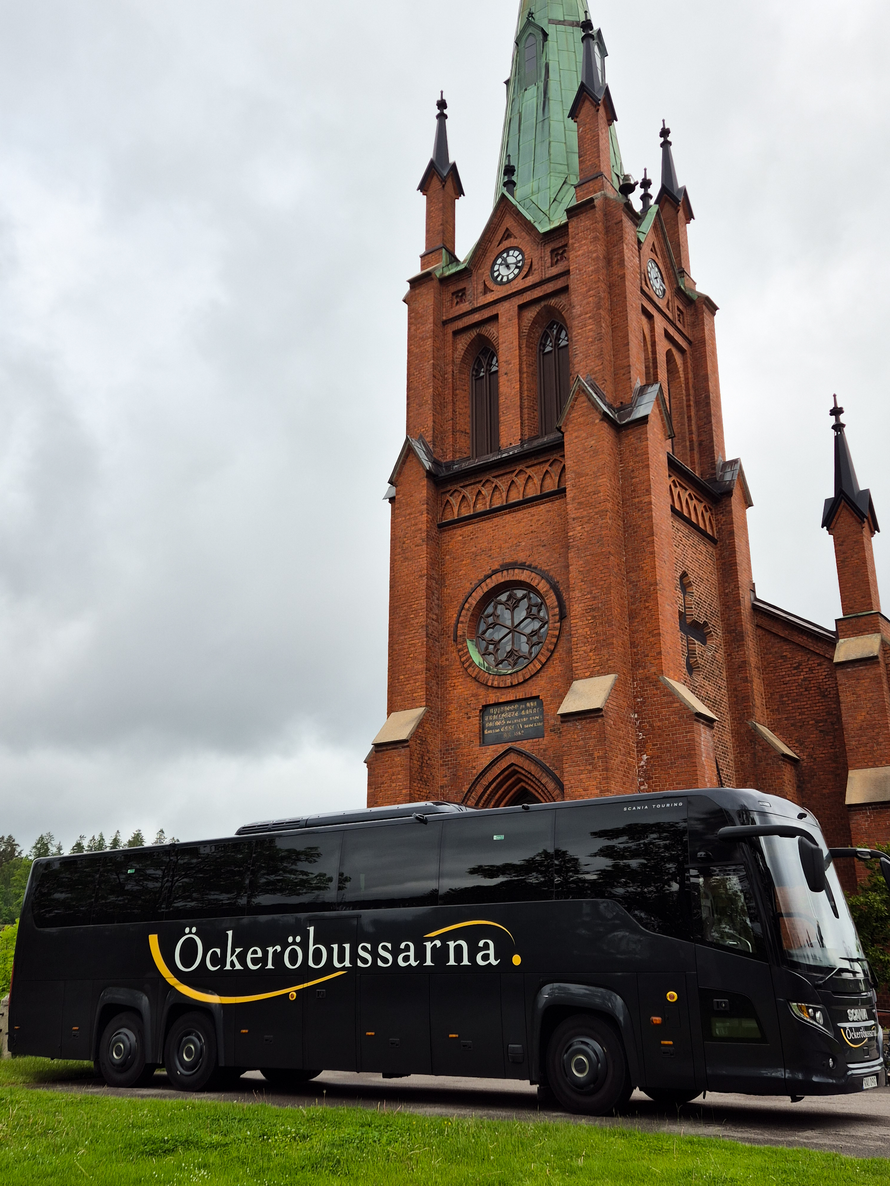 Öckeröbussarnas turistbuss framför en kyrka i rött tegel