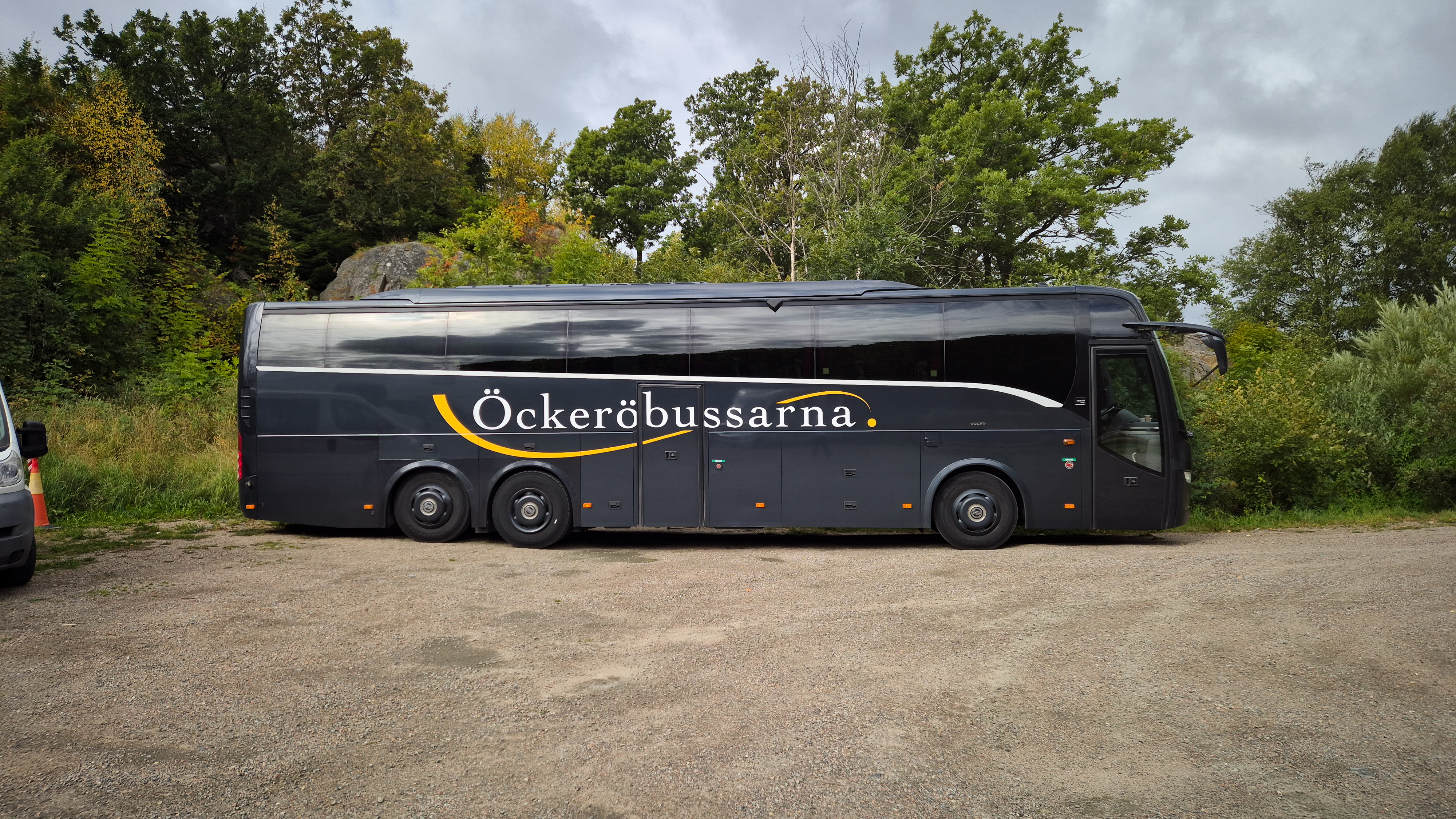 Öckeröbussarnas buss på en grusplan framför träd och klippor