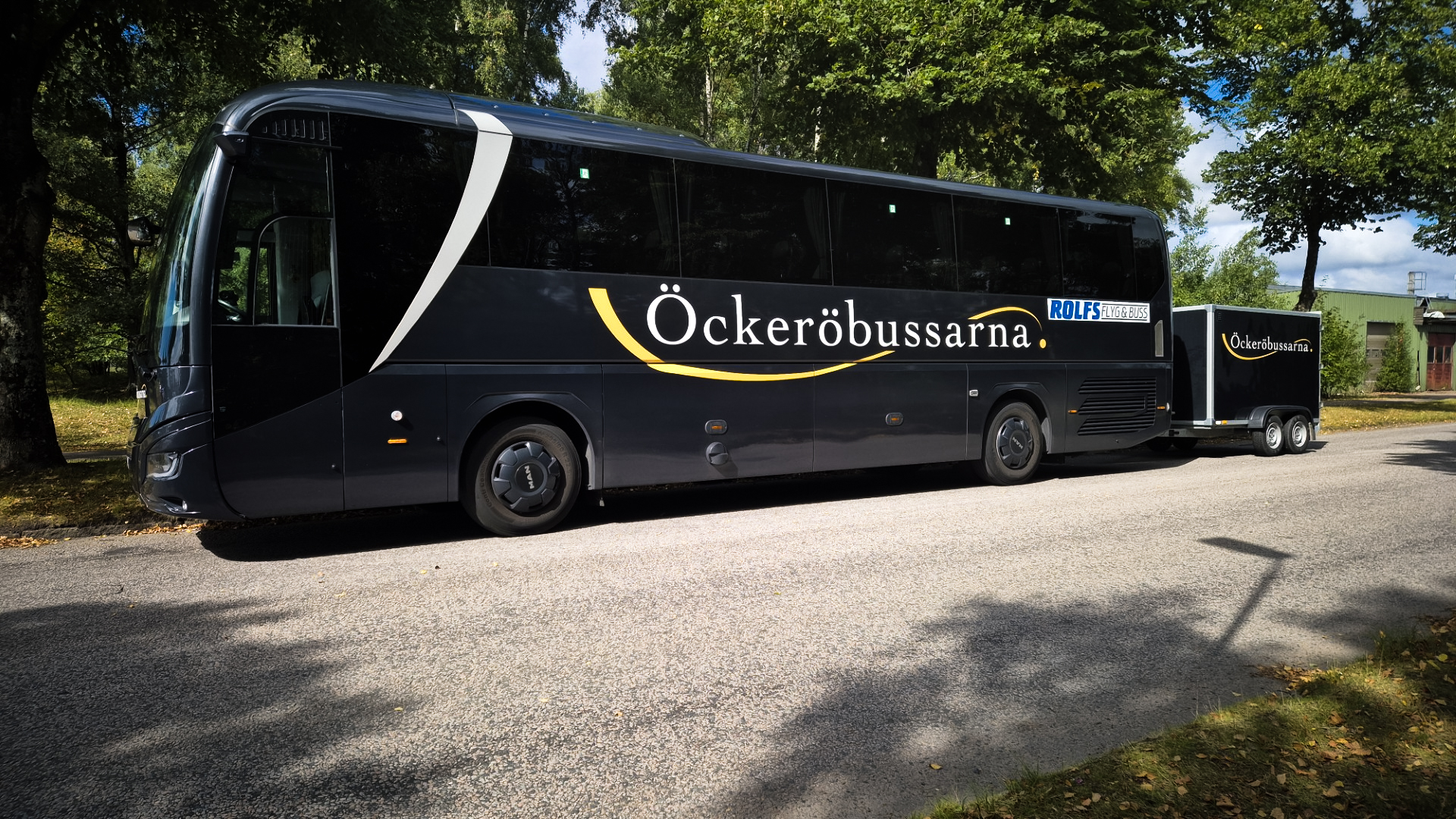 Öckeröbussarnas turistbuss med släpvagn under lummiga träd