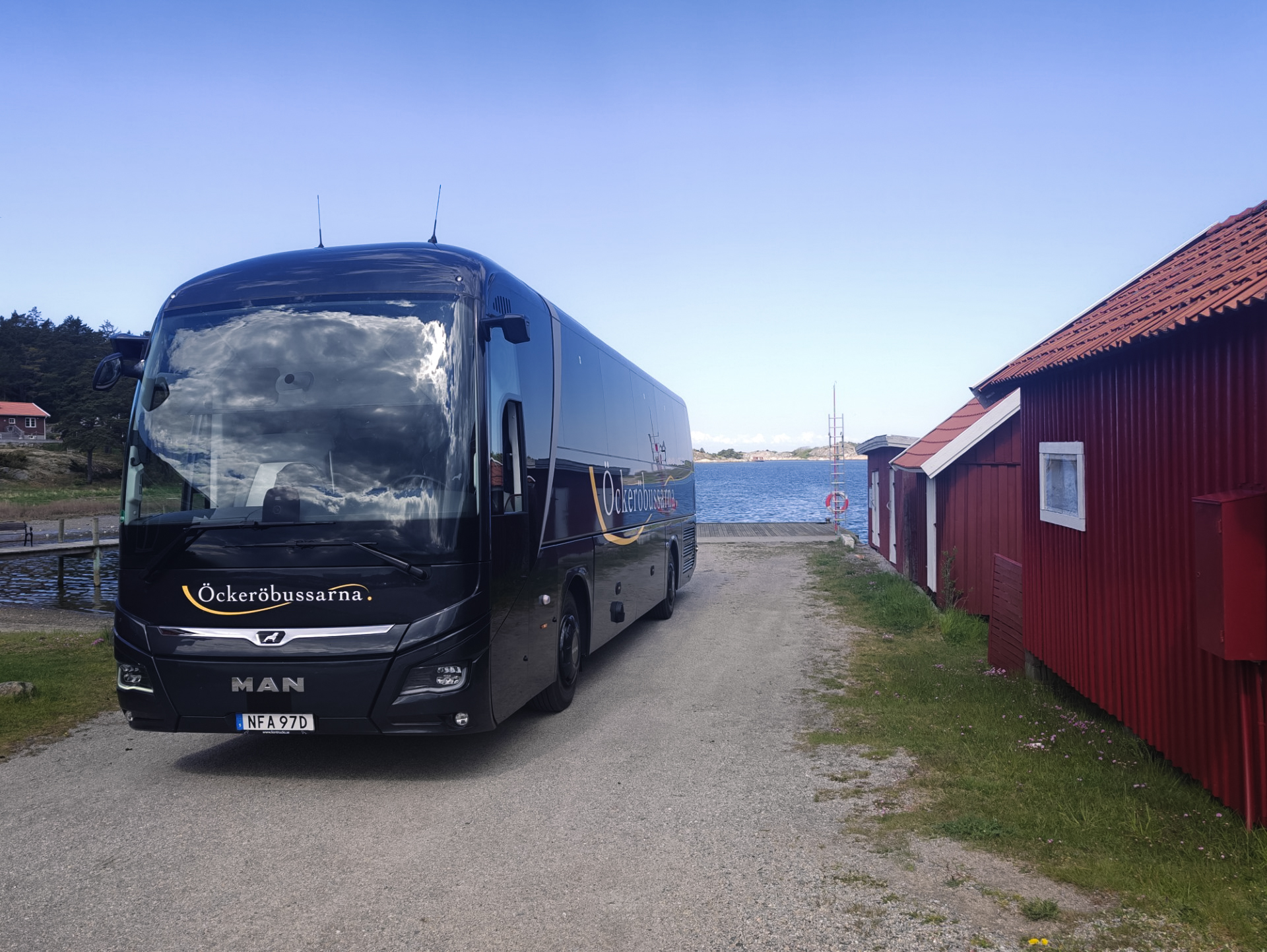 Öckeröbussarnas buss vid en röd sjöbod vid vattnet