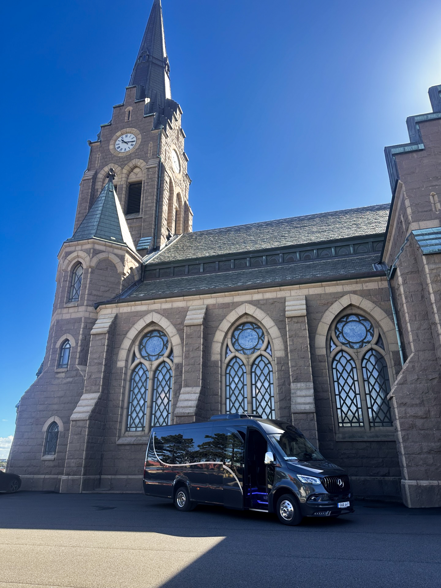 Öckeröbussarnas VIP-buss, en svart Mercedes Sprinter med öppen passagerardörr, framför en stenkyrka.