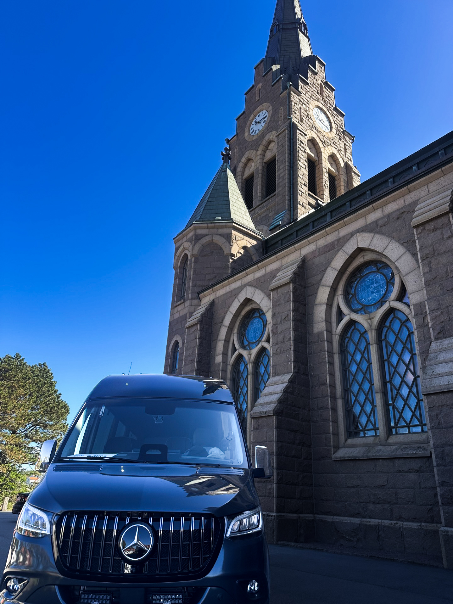 Mercedes Sprinter sedd framifrån, med Mercedes-emblemet och en stenkyrka i bakgrunden.