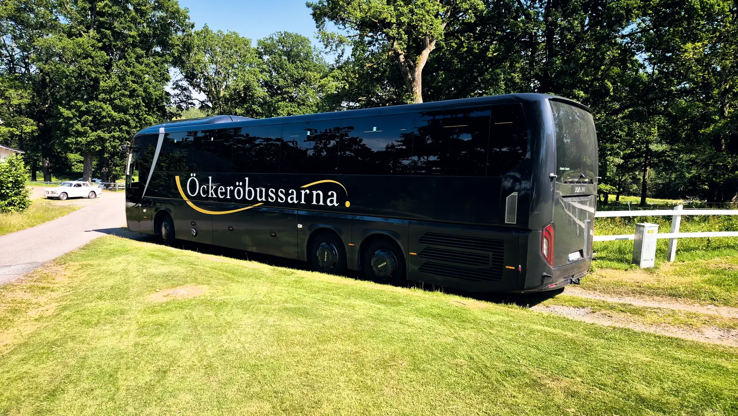 Öckeröbussarnas turistbuss på en solig gräsmatta bland höga träd
