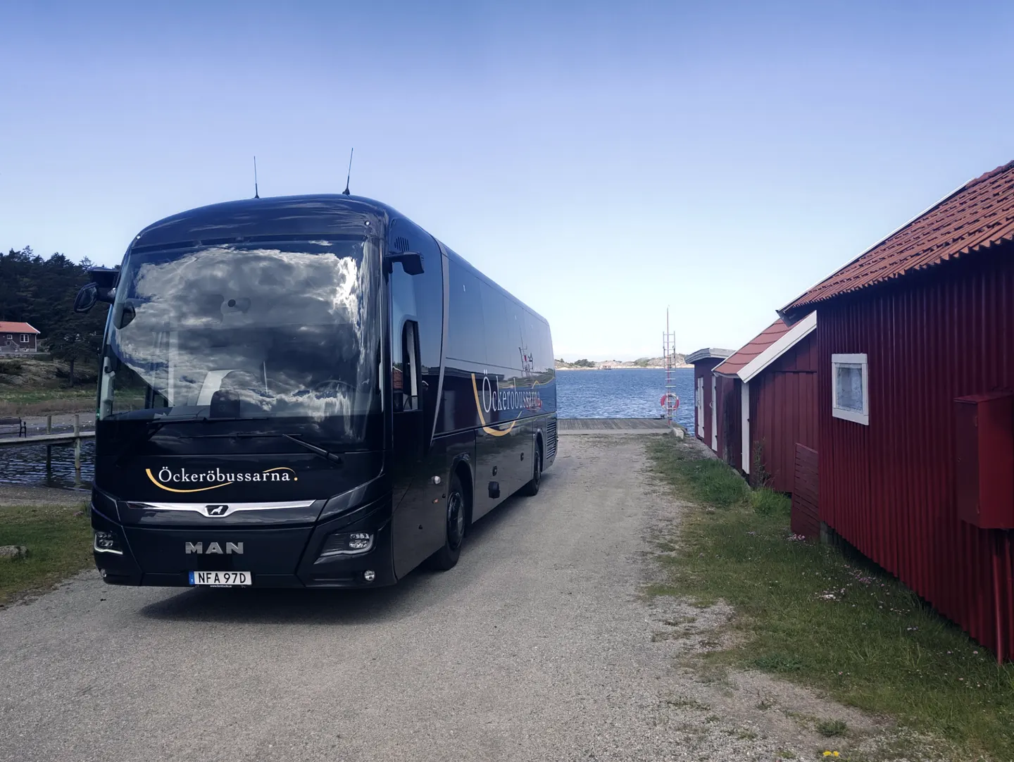 Öckeröbussarnas buss vid en röd sjöbod vid vattnet