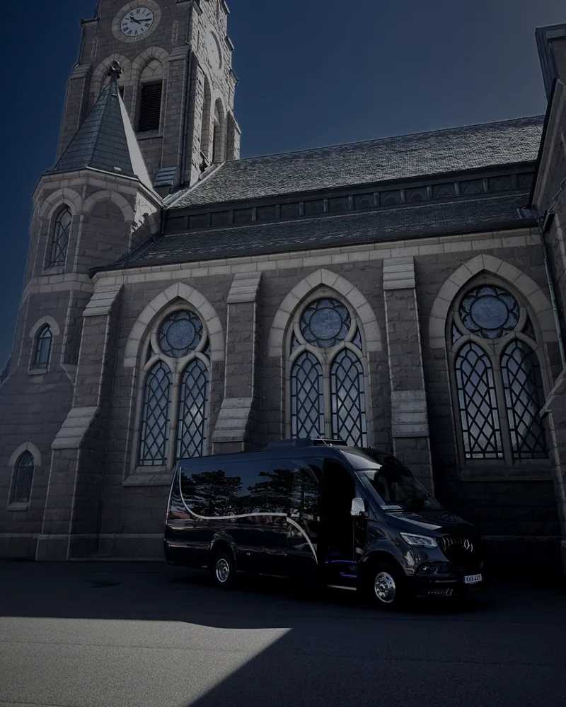En stenkyrka med Öckeröbussarnas svarta Mercedes Sprinter parkerad framför.