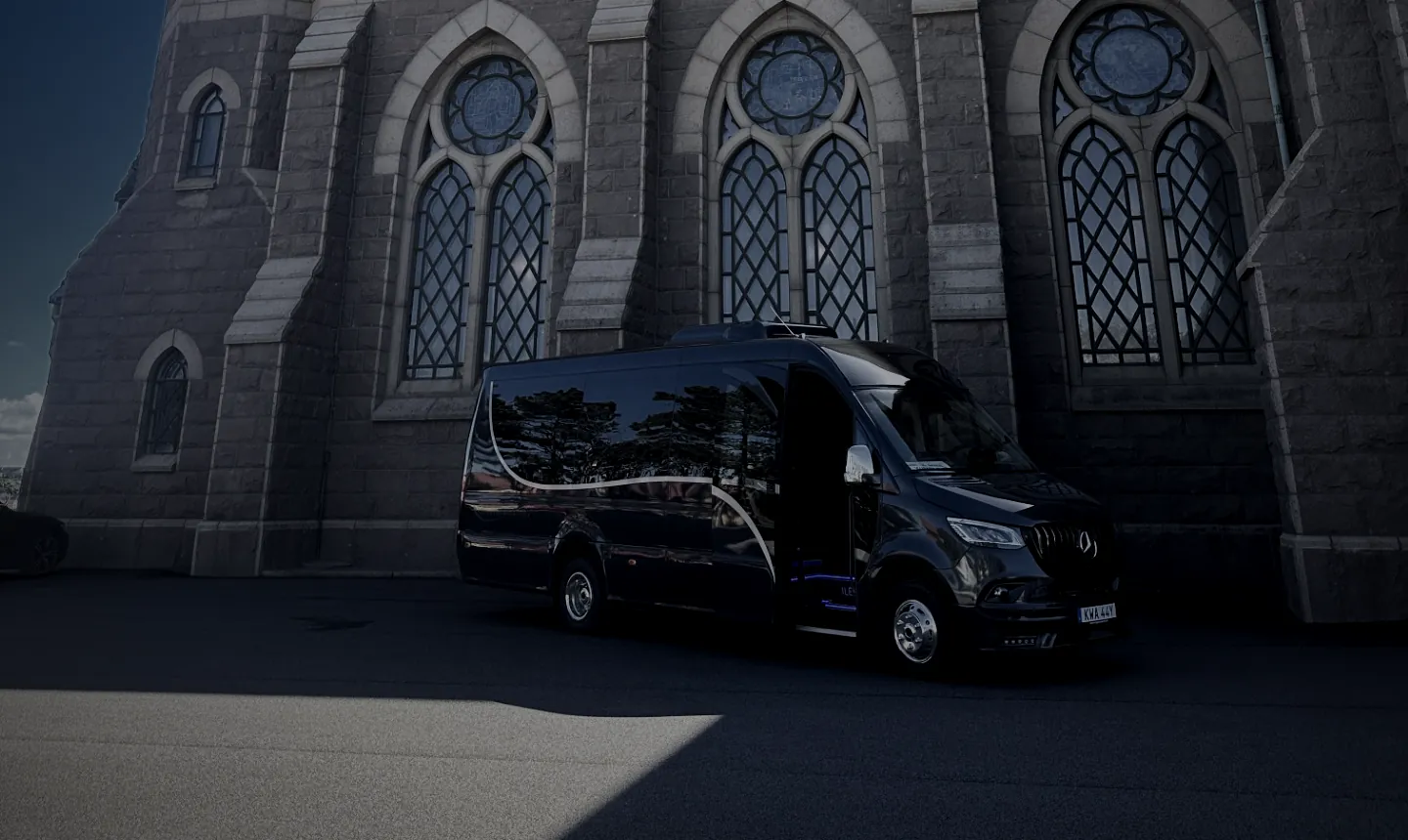 Öckeröbussarnas VIP-buss, en svart Mercedes Sprinter med öppen passagerardörr, framför en stenkyrka.