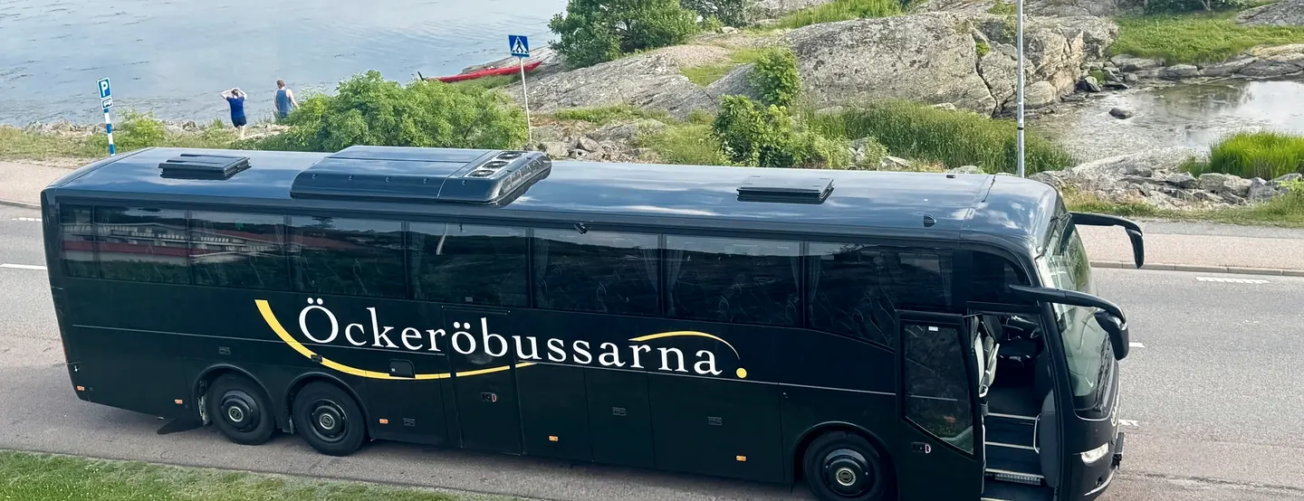Öckeröbussarnas svarta buss vid klippor och vatten i skärgården
