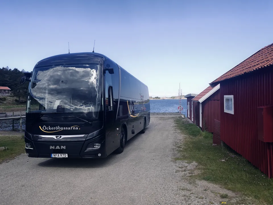 Öckeröbussarnas buss vid en röd sjöbod vid vattnet